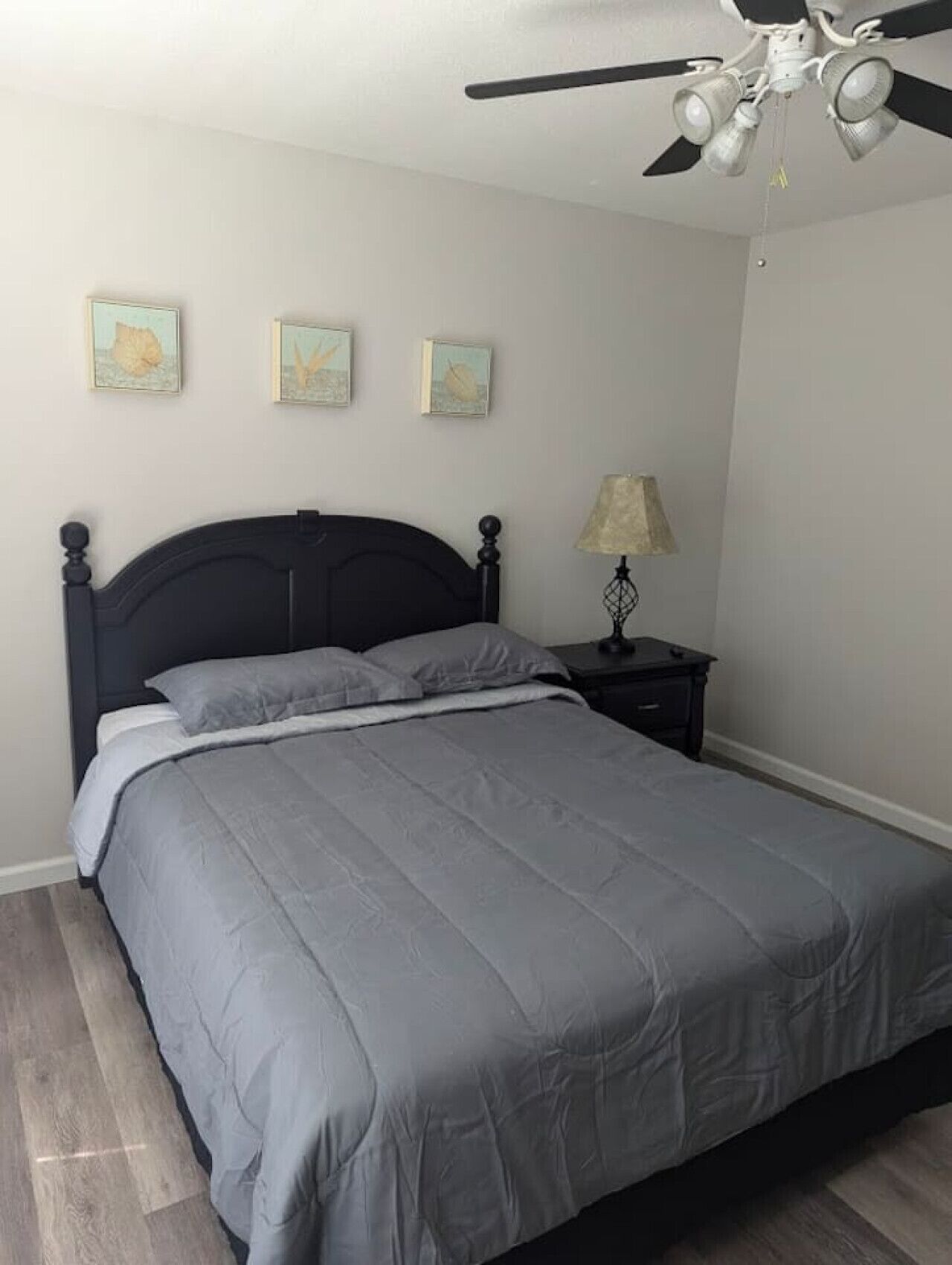 Une chambre à coucher comprenant un lit, une table de chevet, un ventilateur de plafond et trois tableaux accrochés au mur.