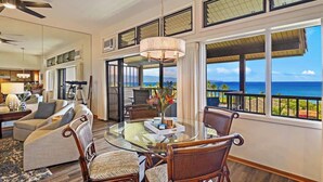 A spacious living room with a glass dining table, comfortable seating, and a large window overlooking the ocean. - Panoramic Ocean View Kapalua Villa #321 (Lahaina)