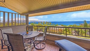 A covered outdoor seating area with a table and chairs, overlooking a scenic view of the ocean and a distant shoreline. - Panoramic Ocean View Kapalua Villa #321 (Lahaina)
