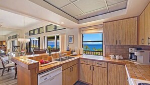 A modern kitchen with wooden cabinets, a built-in dishwasher, and a large window overlooking the ocean. - Panoramic Ocean View Kapalua Villa #321 (Lahaina)