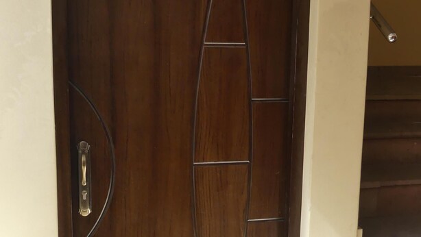 Una porta di legno con un motivo geometrico, una maniglia in metallo e un cartello con un numero sopra.