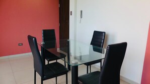 Un tavolo da pranzo con piano in vetro e quattro sedie nere, una parete rossa, una parete bianca e una porta con maniglia.