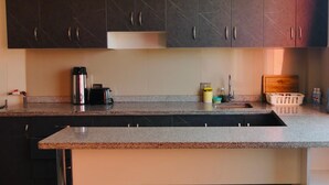 Cucina con mobili scuri, un piano di lavoro in granito, una macchina da caffè, un tostapane, un lavello e un tagliere.