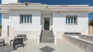 Un edificio moderno con una escalera que lleva a una puerta, asientos exteriores y un muro de piedra.