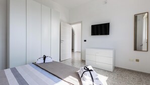 Habitación de hotel con cama, televisor montado en la pared, armario y baño visible a través de una puerta abierta.