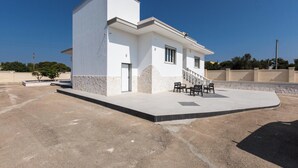 Un edificio moderno con techo plano, una pequeña escalera que conduce a la entrada y un patio empedrado con mobiliario para exteriores.