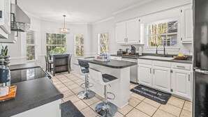 Una cocina moderna con armarios blancos, una isla central con taburetes altos y un rincón para café.