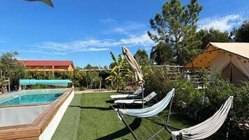 Relax in a serene outdoor space surrounded by lush greenery and trees, featuring a pool, lounge chairs, and a hammock.