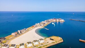 Luchtbeeld van een kustplaatsje met een strand, gebouwen en een pier.