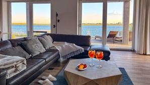 Een moderne woonkamer met een leren bank, een houten salontafel met fruit, en uitzicht op het water door grote ramen.