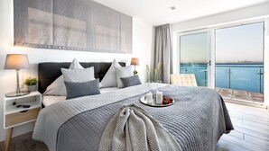 Een moderne slaapkamer met een groot bed, nachtkastjes en uitzicht op de zee vanaf een balkon.