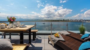 A terrace with a dining table set for two, a wicker sofa, and a view of the sea.