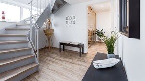 A modern interior with a staircase, a wall-mounted text, a small table, a potted plant, and a decorative boat on a console table.