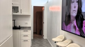 A modern kitchen with white cabinets and a grey tiled floor. There are three bar stools with chrome legs and white seats. A large flat-screen TV is mounted on the wall. - New Furn 1 Br/1 Bath/Kitchen, Manila-Univ Belt, AC, Hot water, Wifi, Netflix -u2 (Manila)