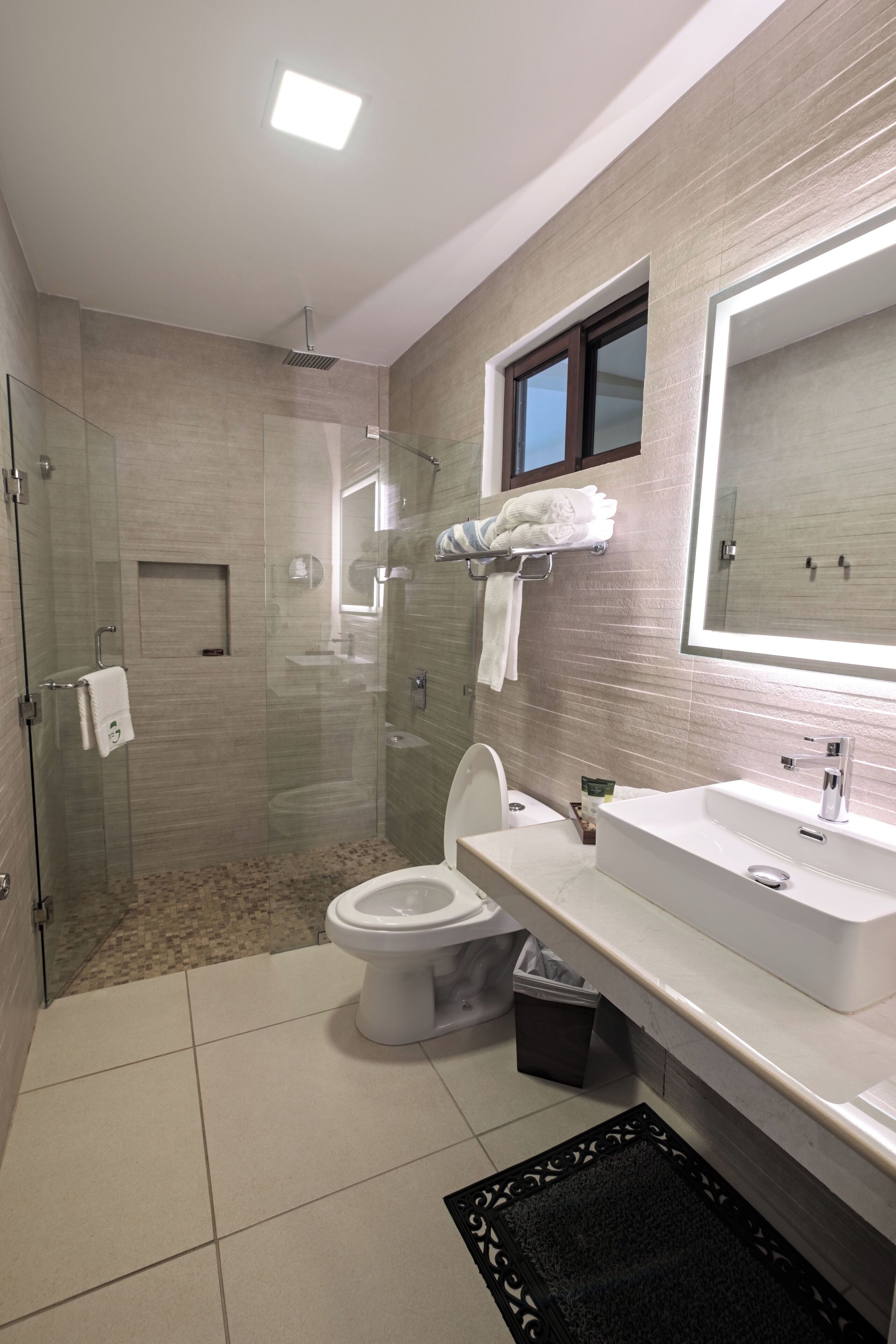 Un bagno moderno con cabina doccia in vetro, un water, un lavandino e un ampio specchio.