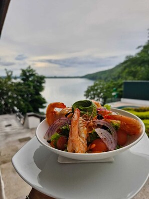 Eine Schüssel Garnelensalat auf einem Tisch mit Blick auf einen See und grüne Vegetation im Hintergrund.