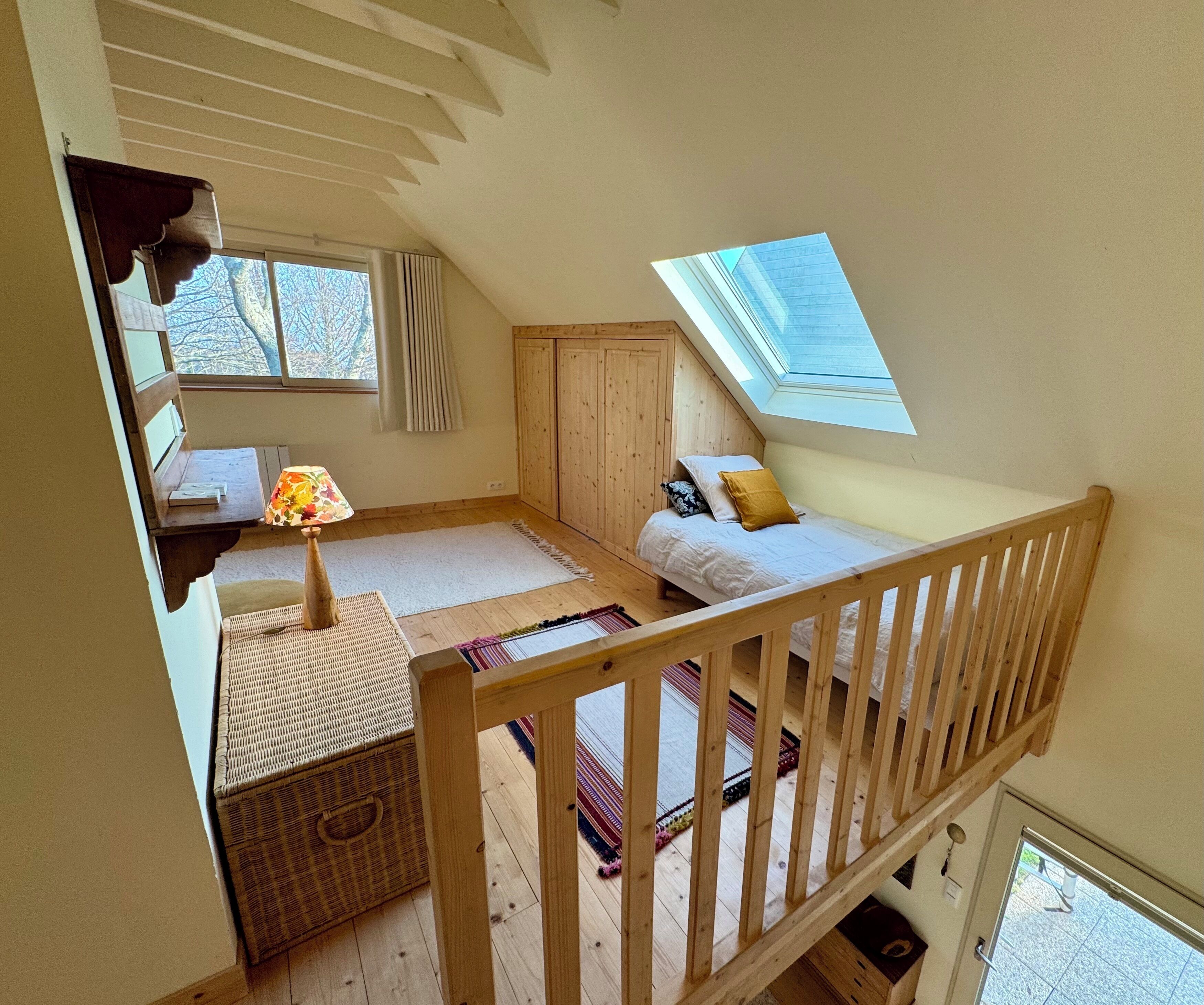 Ein Schlafzimmer im Loft-Stil mit schrägem Dach, einem Oberlicht, einem Bett, einem Schreibtisch und einem Fenster.