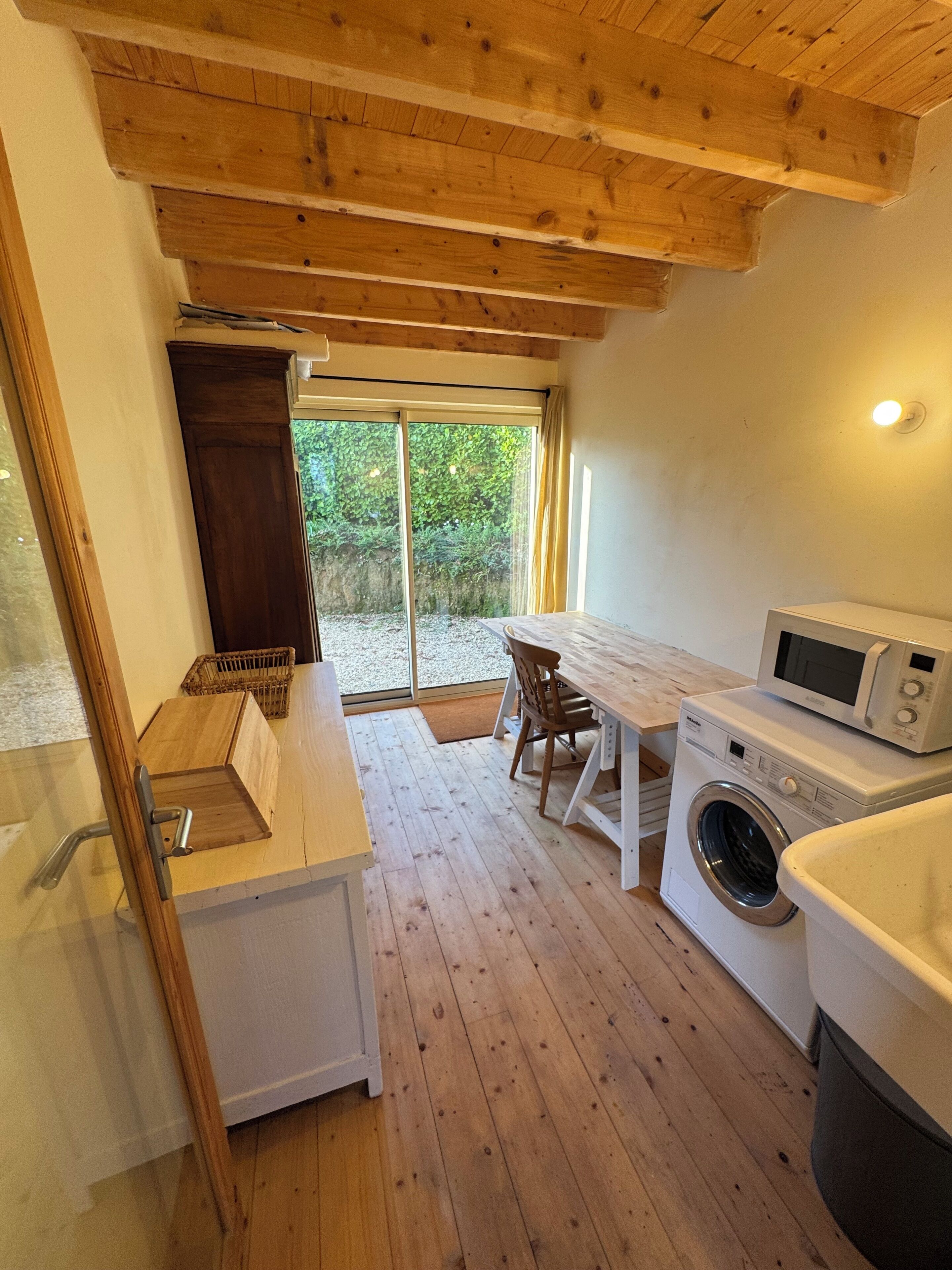 Eine kompakte Küche mit Holzboden, einer Waschmaschine, einer Mikrowelle und einem Essbereich mit Tisch und Stühlen.