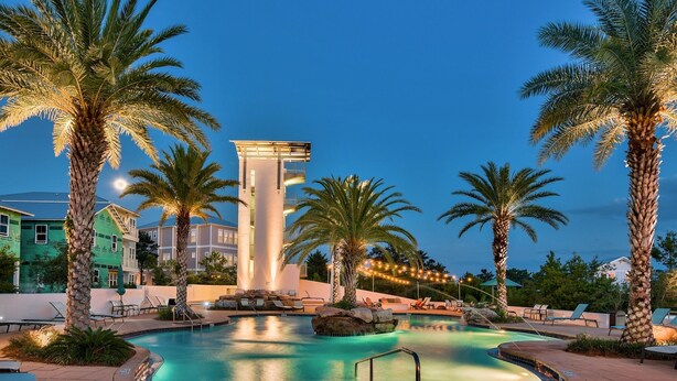 A swimming pool surrounded by palm trees and lounge chairs, with a building in the background. - Tiki Tides on 30A!  Summer dates left!  Golf cart included.  🤩🌴  (Santa Rosa Beach)