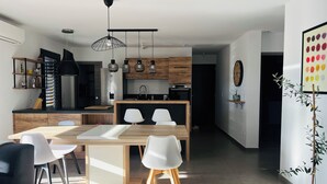 A modern kitchen with a central island, pendant lighting, and a dining area with a sofa and chairs.