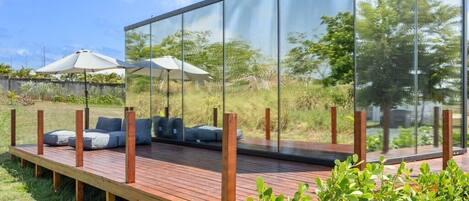 A modern outdoor seating area with a glass enclosure, wooden deck, and outdoor furniture.