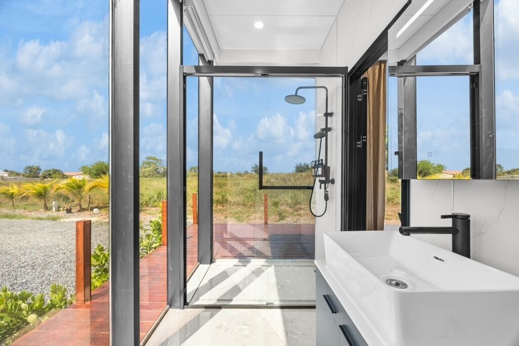 A modern bathroom with a large window, a shower, and a sink.