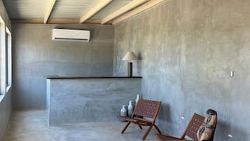 Un intérieur moderne avec un sol en béton, une table ronde en bois, deux chaises en bois, un luminaire suspendu en fibres tressées et un banc intégré avec une lampe.