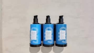 Three blue bottles with black caps labeled 'Dead Sea Essentials' against a plain wall.