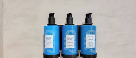 Three blue bottles with black caps labeled 'Dead Sea Essentials' against a plain wall.