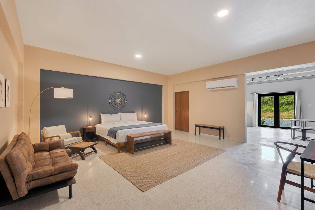 A modern bedroom with a large bed, a brown leather sofa, a small table, and a dining area with chairs.