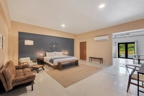 Une chambre moderne avec un grand lit, un canapé en cuir marron, une petite table et un coin repas avec des chaises.