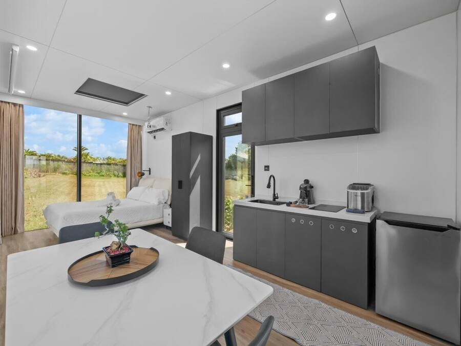 A modern kitchen with grey cabinets, a built-in oven, and a dining area with a white table.