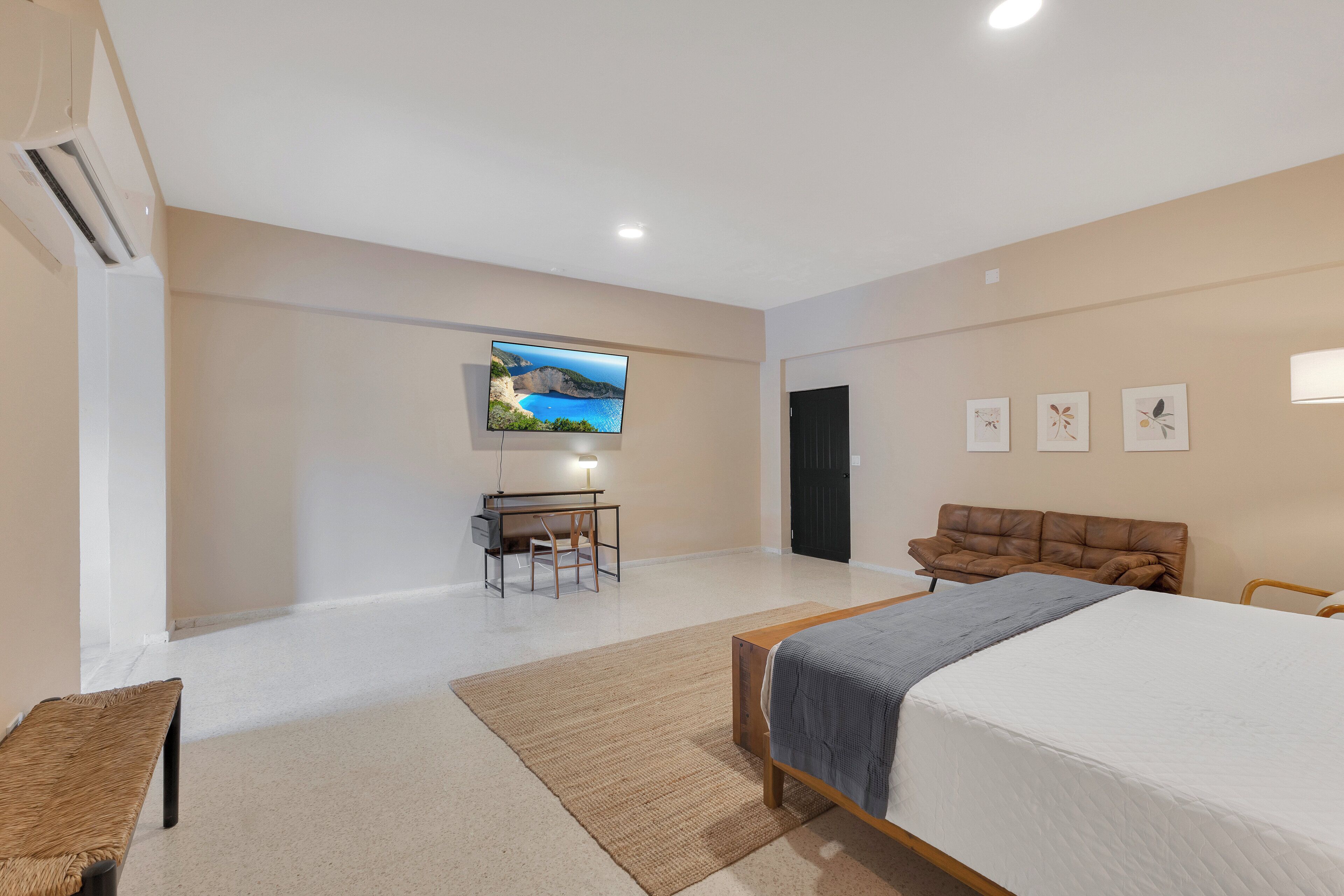 A modern bedroom with a large bed, a desk with a chair, a television, and a brown leather sofa.