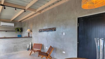 A room with a concrete wall, a wooden chair, a table, a hanging light fixture, and a door.