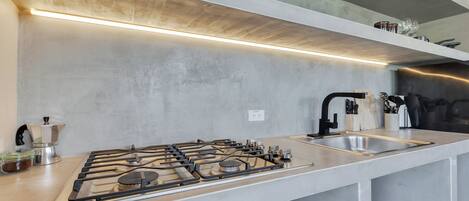 A modern kitchen with a gas stove, stainless steel sink, and overhead lighting.