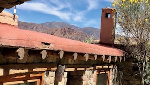 A stone building with a red roof, a chimney, and a window with a curtain. - HOSTERIA REFUGIO DEL PINTOR (Tilcara)