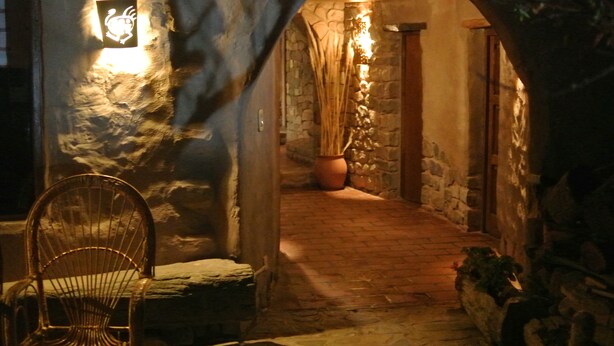 A stone-walled corridor with a rustic chair and a potted plant. - HOSTERIA REFUGIO DEL PINTOR (Tilcara)