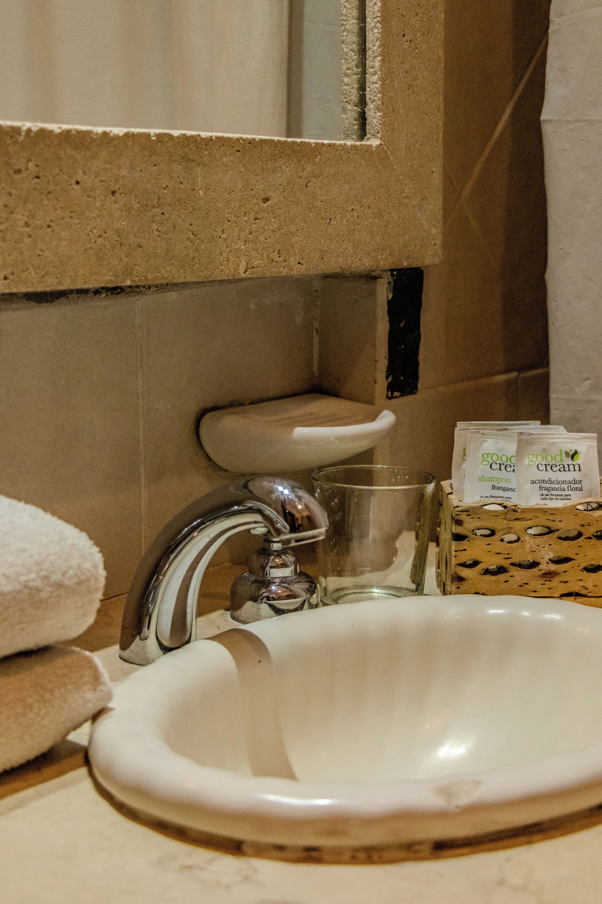 Un lavabo dans la salle de bain, avec un miroir au-dessus, une serviette et un verre d’eau.