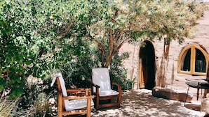 An outdoor seating area with two wooden chairs and a table, surrounded by lush greenery and a stone wall. - HOSTERIA REFUGIO DEL PINTOR (Tilcara)