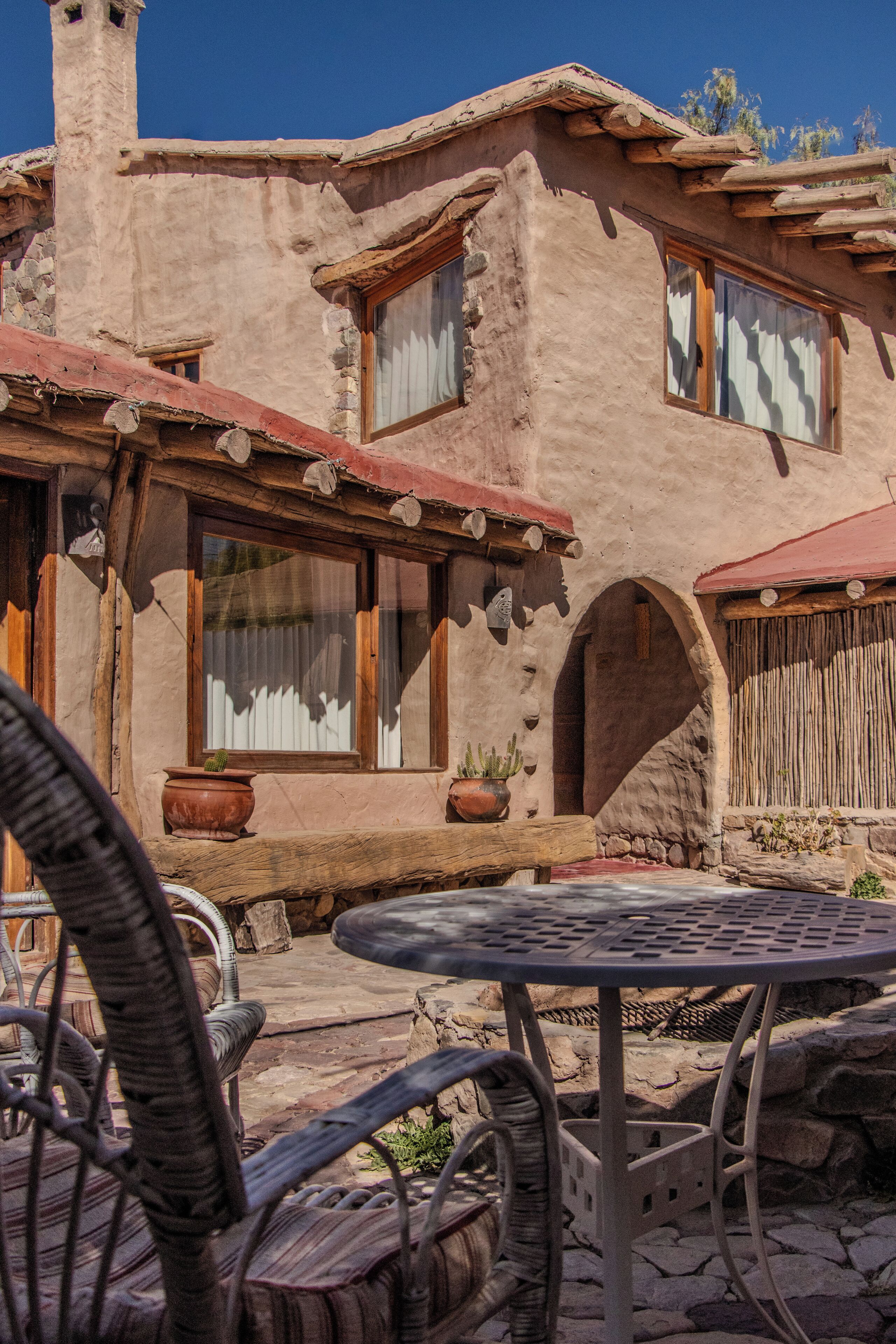 A rustic building with a stone facade, wooden windows, and a patio area with wicker furniture and a metal table.