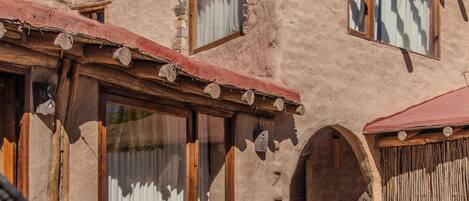 A rustic building with a stone facade, wooden windows, and a patio area with wicker furniture and a metal table.