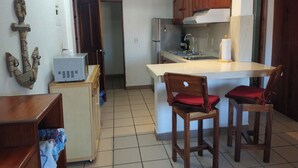 Cocina compacta con armarios de madera, un refrigerador pequeño y piso de baldosas.