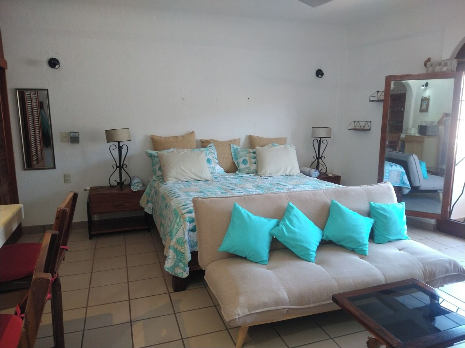A bedroom with a bed, a sofa, a table, and a mirror.