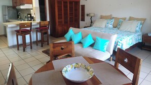 Habitación de hotel compacta con kitchenette, una cama con muchas almohadas, una mesa de comedor con sillas y un ventilador de techo.