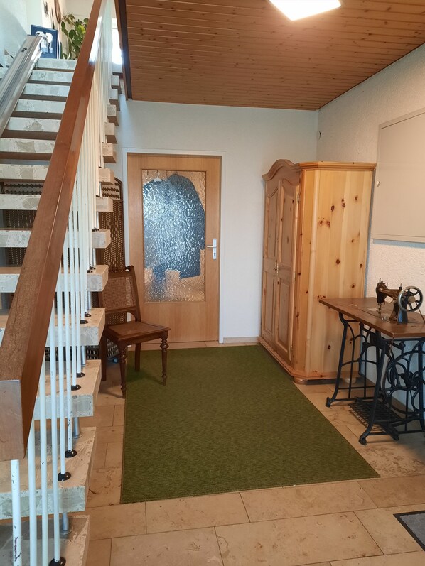 A staircase with a wooden railing, a door with a frosted glass panel, a wooden cabinet, and a sewing machine on a table.