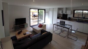 Un espacio habitable moderno con sofá, mesa de centro, televisor y una mesa de comedor de vidrio.