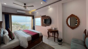 Habitación de hotel con cama, ventilador de techo, televisor, espejo y vista al mar.