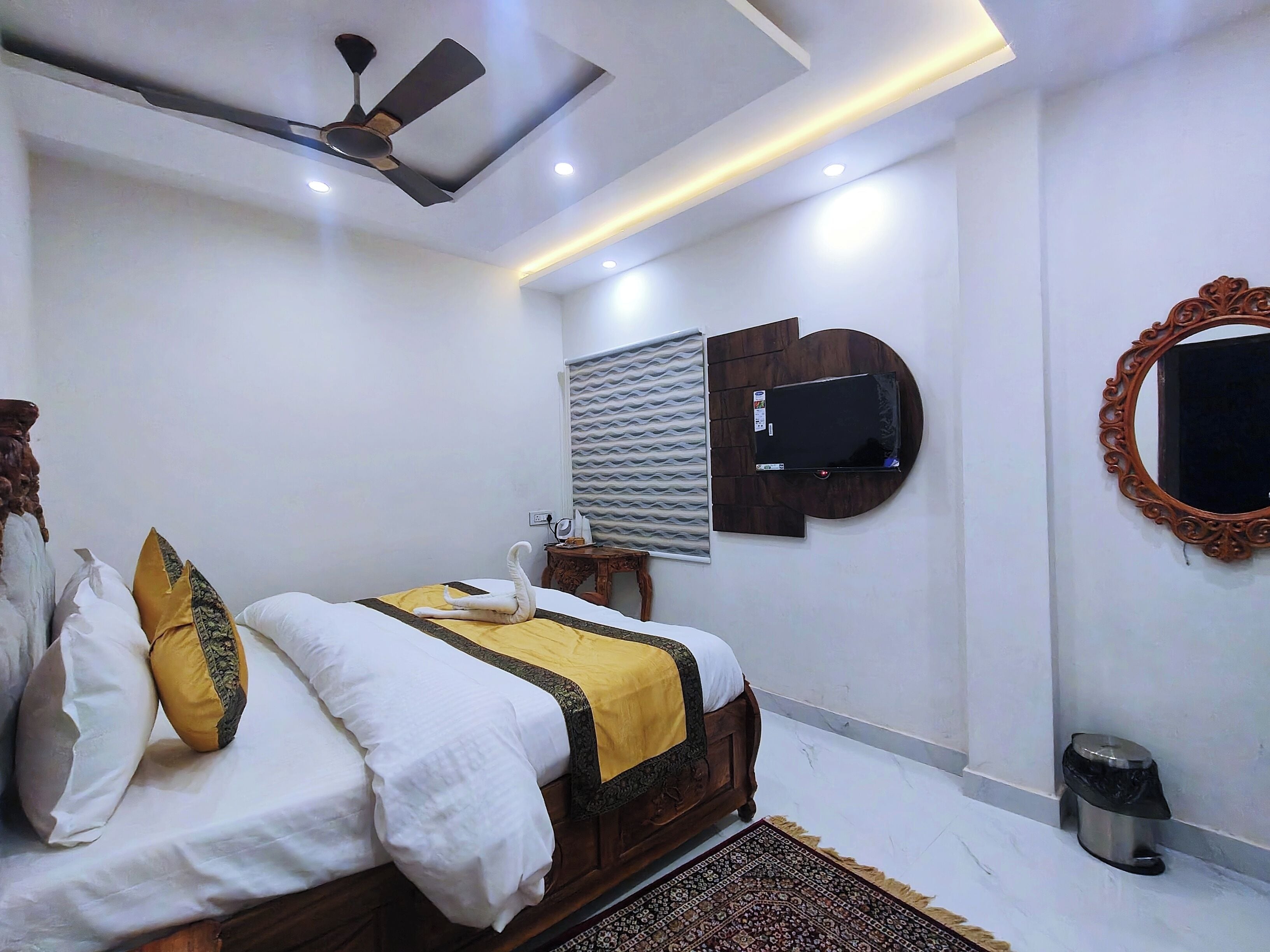A modern bedroom with a bed, a ceiling fan, a TV mounted on the wall, and a decorative mirror.