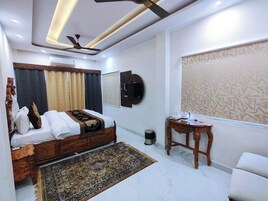 Una camera d'albergo moderna con un letto grande, una ventola a soffitto, un televisore fissato al muro e un tavolino con un bollitore.