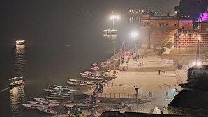 Vista nocturna de un muelle ribereño con barcos, un puente y un edificio iluminado al fondo.